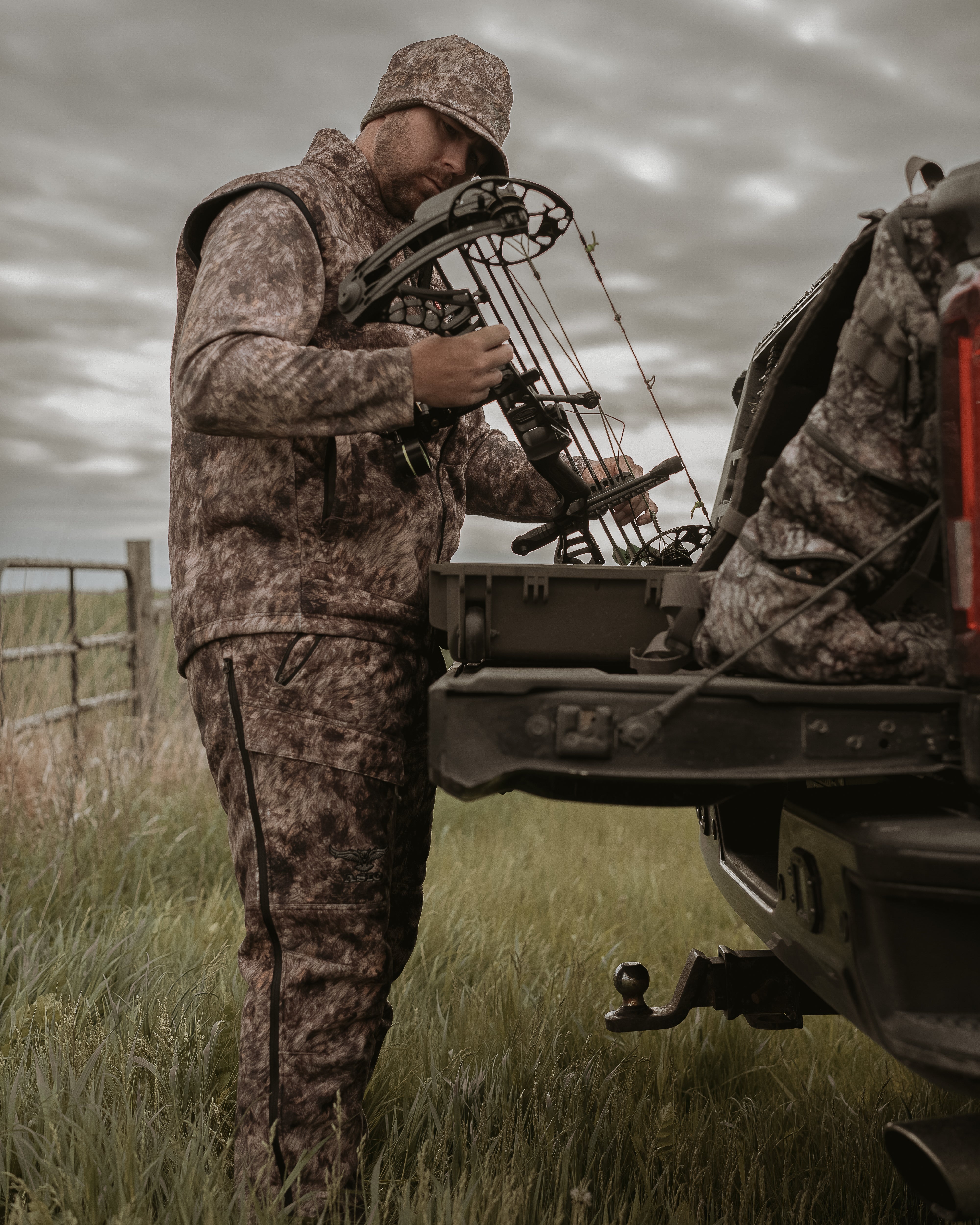 Bowhunter wearing ASIO Gear Heavyweight Vest in RAPX CAMO® while gearing up at the truck—built for late-season performance and cold-weather stealth.