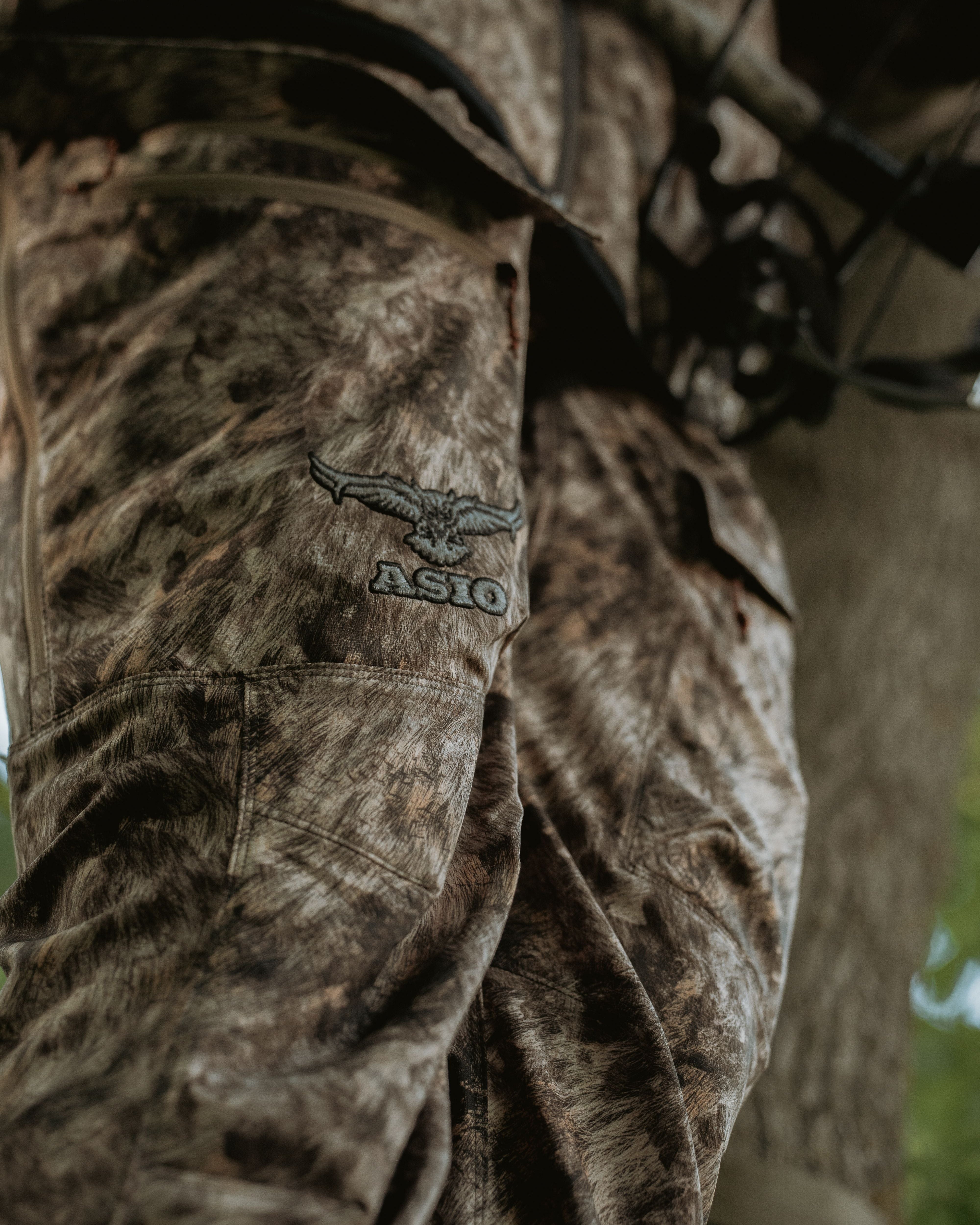 Close-up of ASIO Gear lightweight early season pant in RAPX camo showing embroidered logo and pocket details in treestand setup