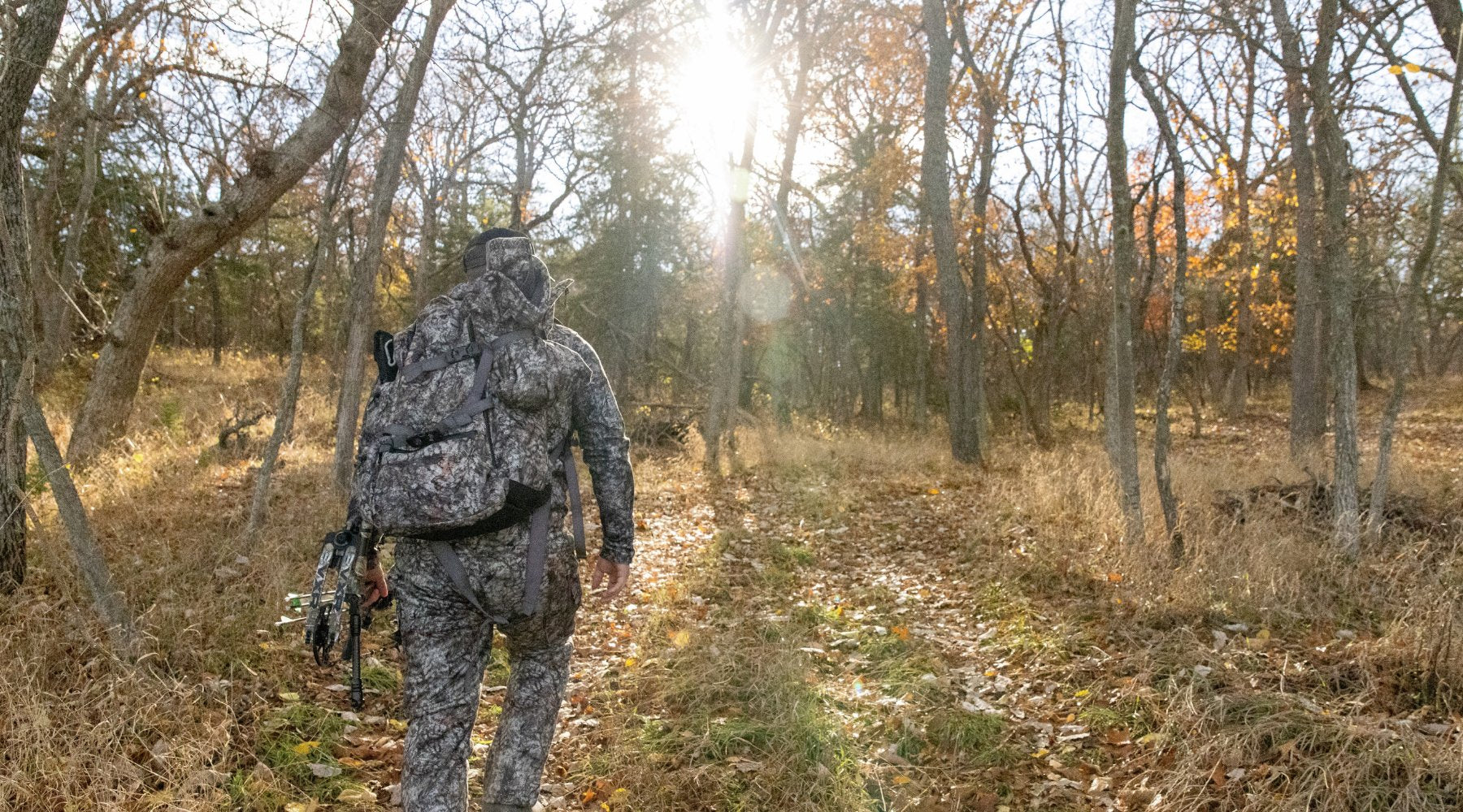 asio gear hunter wearing a full set of raptor camo walks into the woods for a hunt during the whitetail rut.