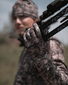 Hunter in ASIO RAPTOR camo with bow over shoulder wearing lightweight stretch gloves during active early season hunt