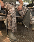 Hunter seated on tailgate wearing RAPX camo Midweight Sherpa Pants showing full-length zippers for ventilation and layering.